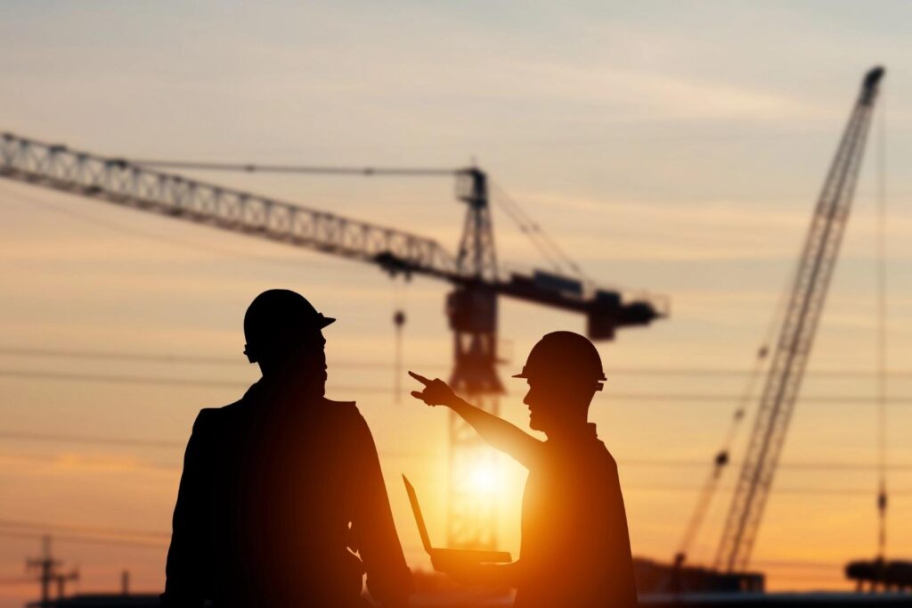 silhouette of construction workers with large rig in the background